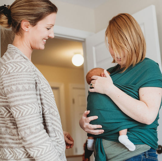 a postpartum doula supports a postpartum client with their newborn baby as they learn how to use a baby wrap